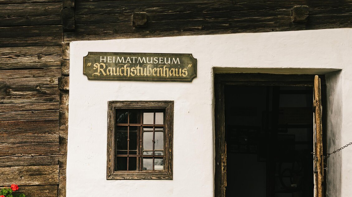 Ein traditionelles Haus mit einem Schilder des Heimatmuseums "Rauchstubbenhaus". Es zeigt schöne Blumen und Holzdetails an der Fassade. | © Oststeiermark Tourismus