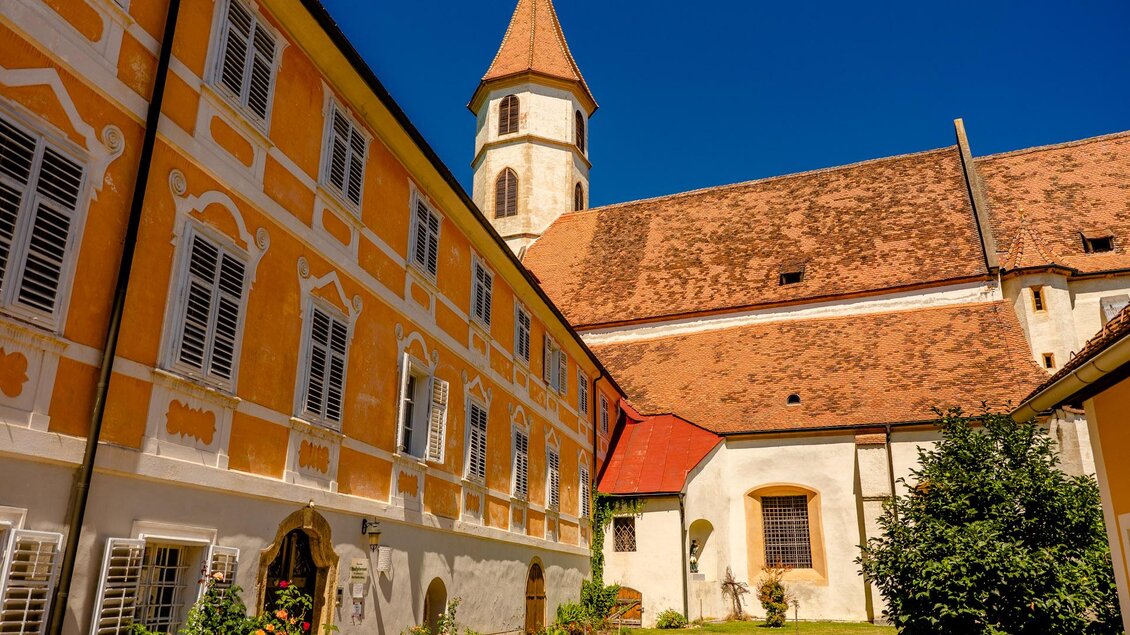 Historische Gebäude und Kirche mit rotem Ziegeldach und Kirchturm in einem begrünten Innenhof der Altstadt von Bad Radkersburg. | © Zehnerhaus Bad Radkersburg