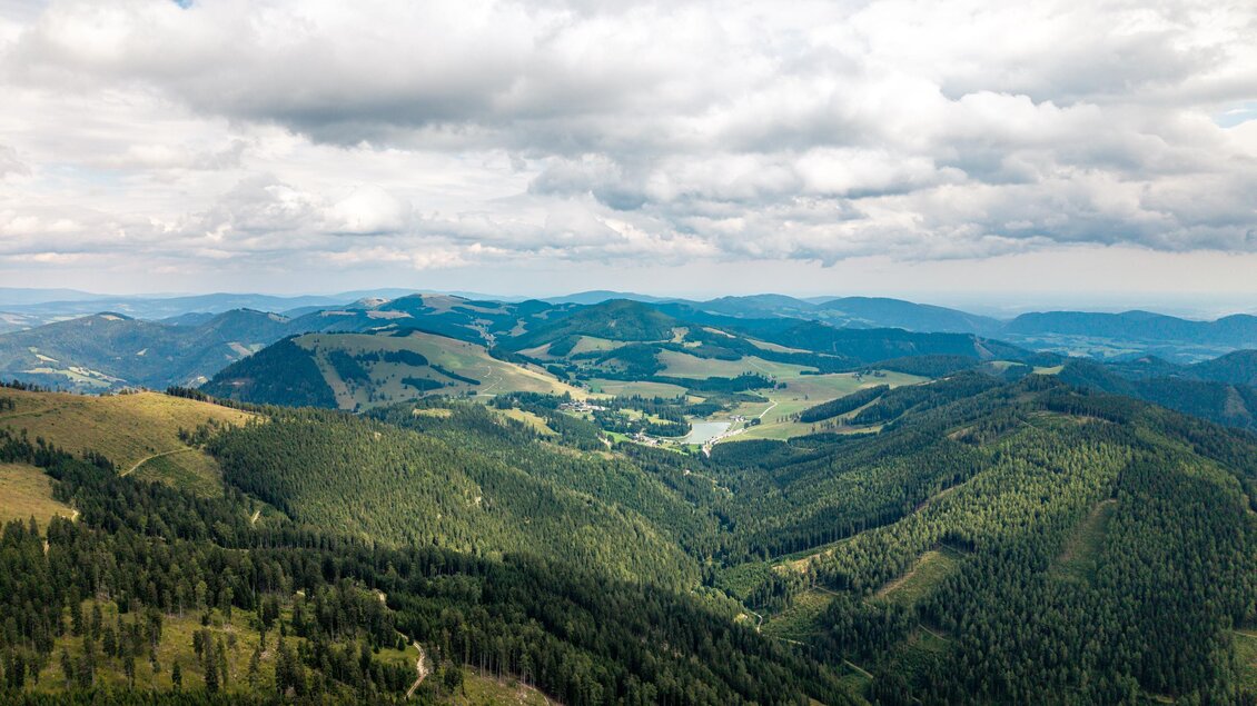 Eine weitläufige Berglandschaft mit sanften Hügeln und dichten Wäldern. Der Himmel ist bewölkt und es gibt weite grüne Täler in der Ferne. | © Oststeiermark Tourismus