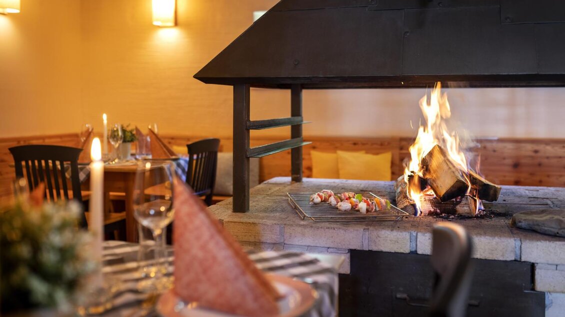 Ein einladender Innenraum mit einem gemütlichen Kaminfeuer. Auf dem Tisch stehen gedeckte Plätze und eine schöne Tischdekoration. | © Jufa Hotel Eisenerz