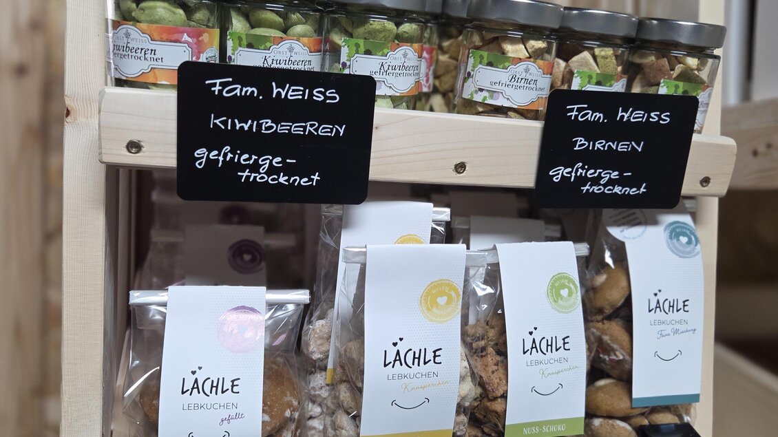 Eine Holzkonstruktion mit verschiedenen Gläsern und Tüten voller Snacks. Die Produkte sind liebevoll beschriftet und repräsentieren lokale Köstlichkeiten. | © Karl August