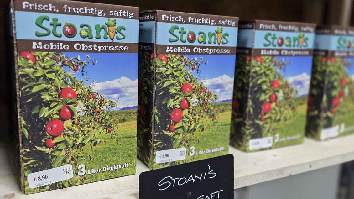 Kisten mit Apfelsaft von "Stoani's" stehen auf einem Regal. Die Verpackungen zeigen frische Äpfel und eine malerische Landschaft. | © Karl August