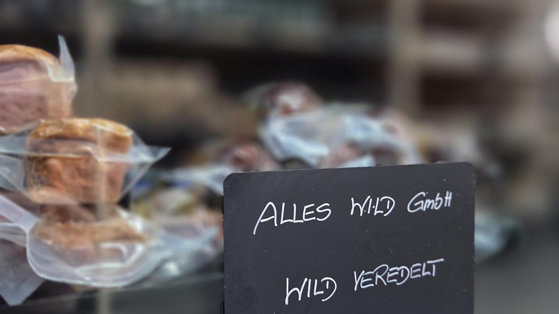 Ein Verkaufstisch mit verschiedenen Fleischwaren ist sichtbar. Ein Schild zeigt den Hinweis "Alles wild gerichtet". | © Karl August