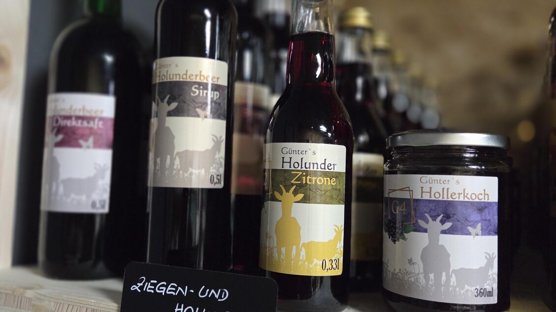 Eine Regale mit verschiedenen Flaschen und Gläsern, die Holunderprodukte zeigen. Darunter steht ein Schild mit der Aufschrift "Ziegen- und Holunderhof". | © Karl August