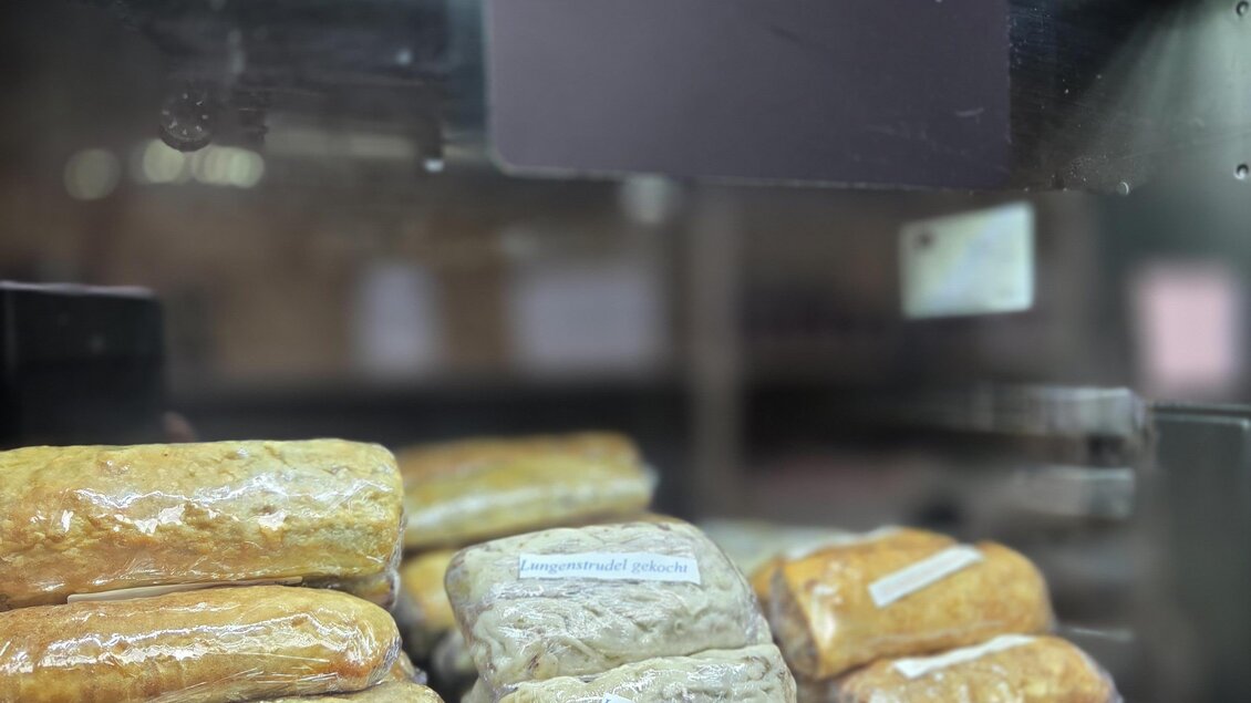Eine Auslage mit verschiedenen Brötchen und Gebäckstücken. Darüber hängt ein Schild mit der Aufschrift "Familie Kranz" und "Suppeneinlagen". | © Karl August