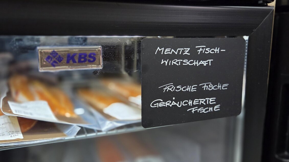 Ein Kühlschrank mit verschiedenen Stücken geräucherter Fisch. Darauf steht "Mentz Fischwirtschaft" und "frische Produkte". | © Karl August