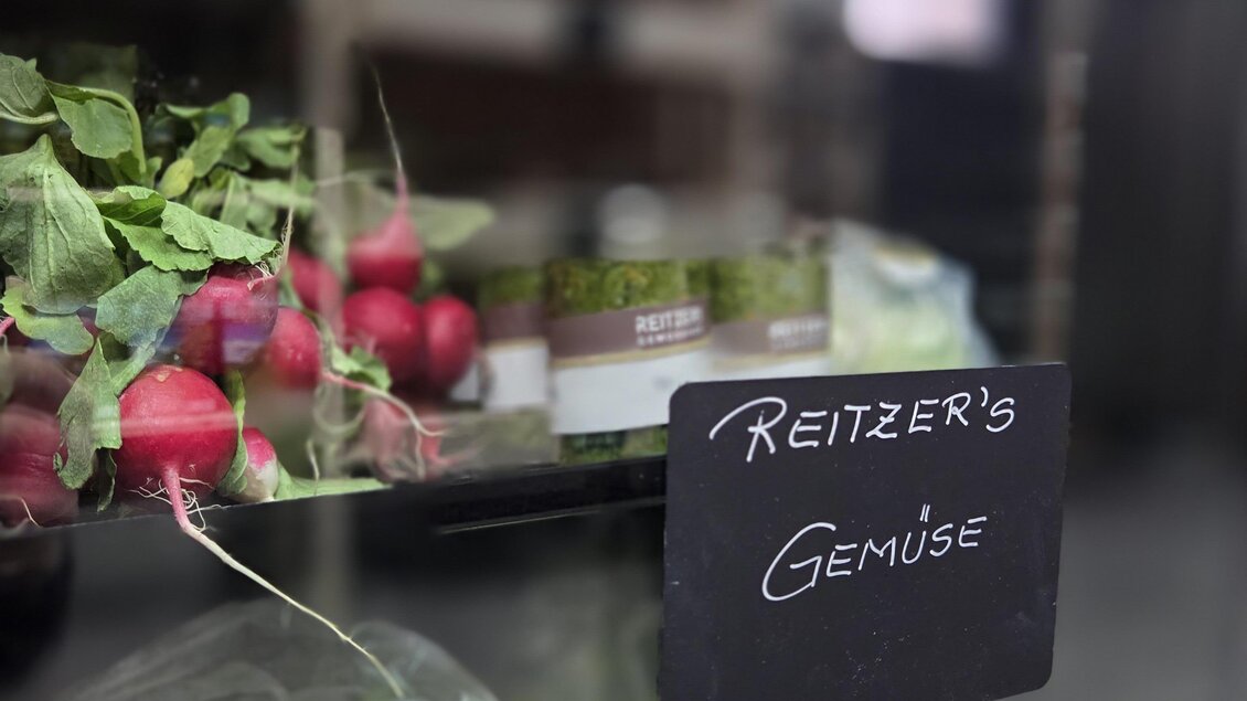 Frisches Gemüse in einem Glasregal mit Radieschen, Salat und Kraut. Eine Tafel zeigt "REITZER'S GEMÜSE". | © Karl August