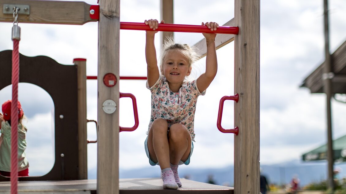 <p>Ein fröhliches Kind spielt am Spielplatz am Loser und zieht sich an einer Stange am Klettergerüst hoch. Im Hintergrund ist der Start der Rutsche und ein Schirm der Loseralm sichtbar.</p> | © TVB Ausseerland-Salzkammergut | Tom Lamm