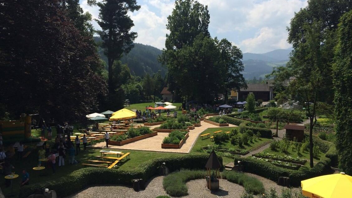 Ein schöner Garten mit bunten Sonnenschirmen und viel Grün. Im Hintergrund sind Gäste zu sehen, die die Natur genießen. | © Anita Fössl