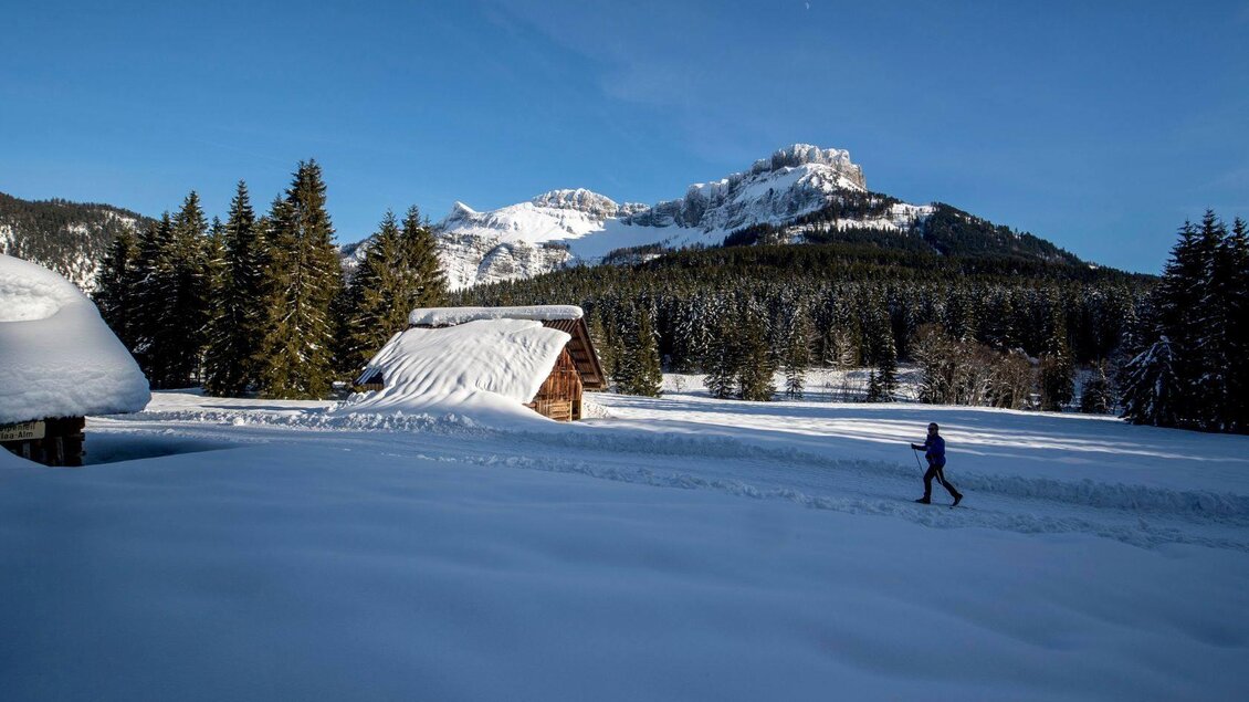 <p>Die winterliche Landschaft mit schneebedeckten Hütten und Tannenbäumen bei der Blaa Alm in Altaussee. Im Hintergrund ist der Loser unter klarem blauen Himmel zu sehen, während eine Person im Schnee langläuft.</ | © TVB Ausseerland - Salzkammergut-Tom Lamm