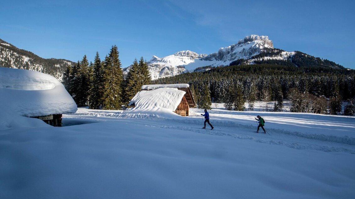 <p>Schneebedeckte Berglandschaft des Ausseerlandes mit Hütten und dem Loser im Hintergrund. Zwei Personen sind beim Langlaufen im Schatten zu sehen.</p> | © TVB Ausseerland - Salzkammergut-Tom Lamm