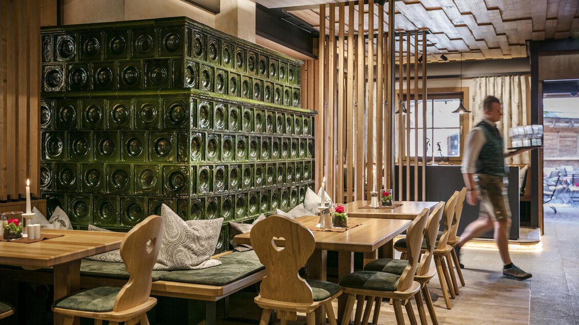 Ein modernes Restaurant mit Holzmöbeln und einer grünen Glaswand. Im Hintergrund sieht man einen Gast, der sich bewegt. | © Latschenhütte
