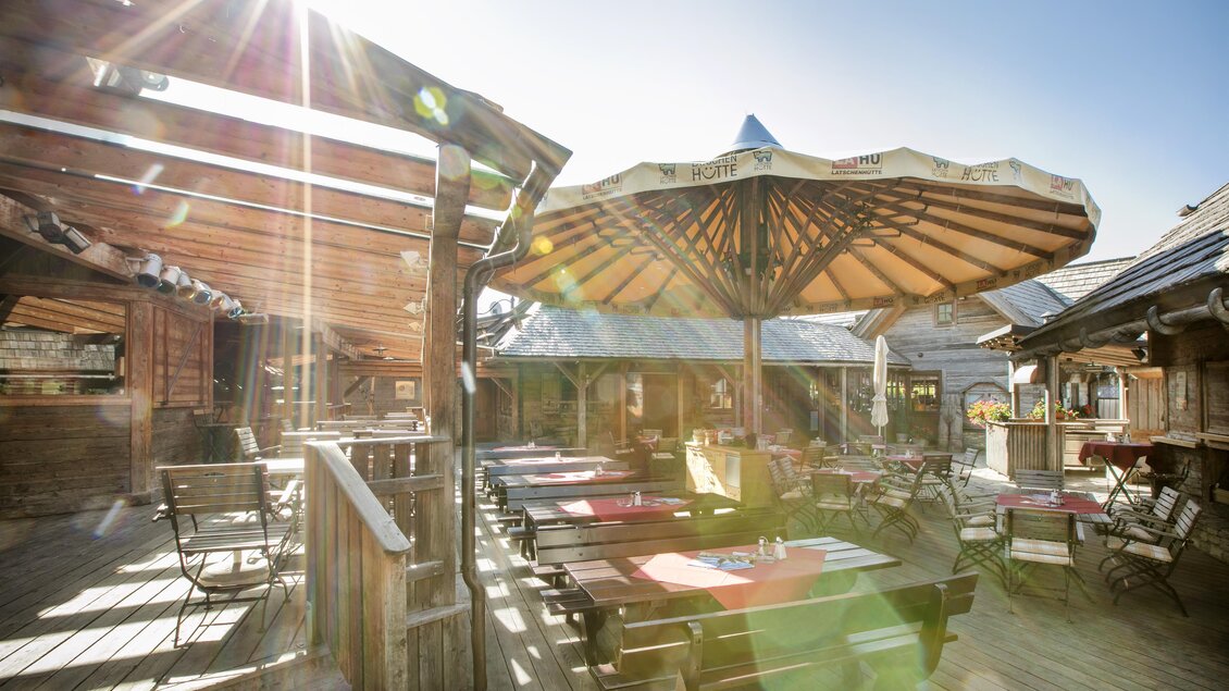 Eine sonnige Terrasse mit Tischen und Stühlen unter einem großen Sonnenschirm. Die Atmosphäre ist einladend und freundlich. | © Latschenhütte