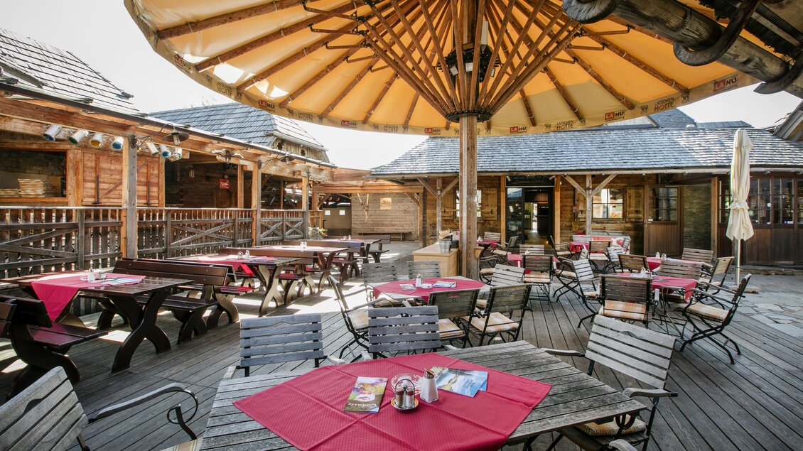 Eine einladende Terrasse mit Holzstühlen und roten Tischdecken. Sonnenschirme bieten Schatten in der entspannten Atmosphäre. | © Latschenhütte