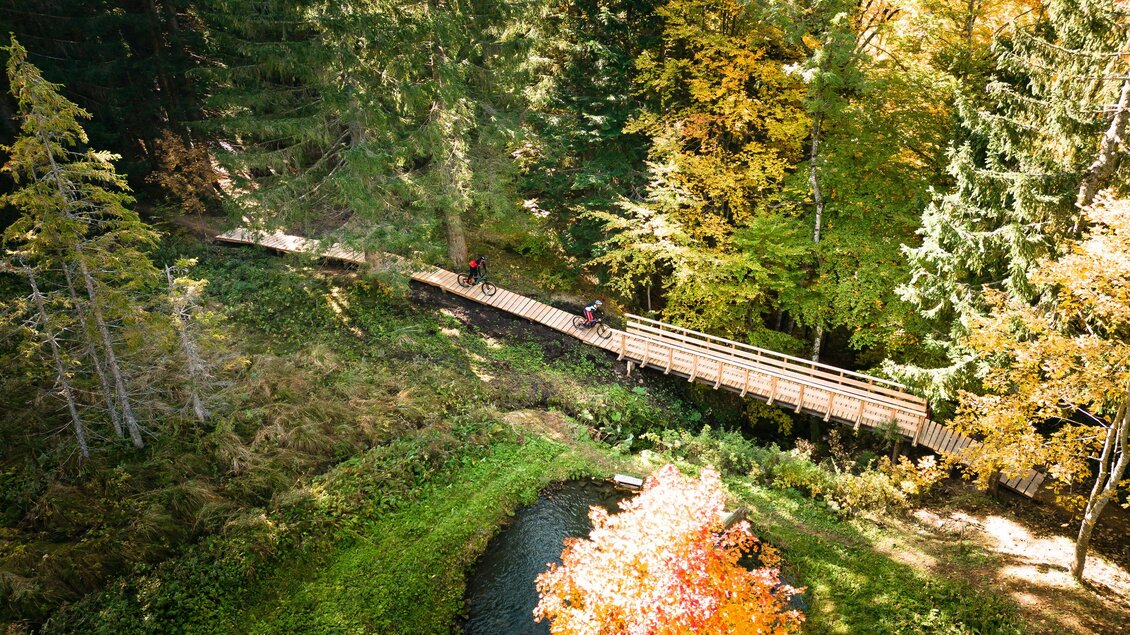 <p>Eine Holzbrücke führt am Augst Trail durch den bunten Wald am Loser in Altausse. Darunter fließt ein ruhiger Bach inmitten der Natur.</p> | © Loser Bergbahnen Altaussee/K. Steinegger