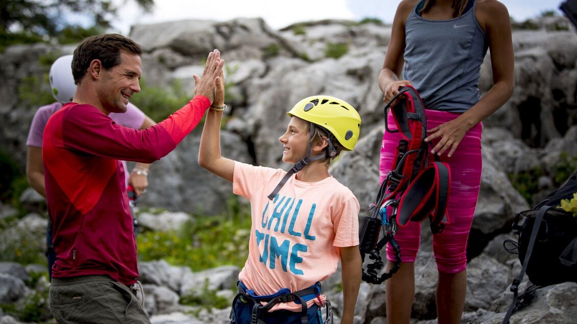 <p>Ein Kind mit einem Kletterhelm gibt einem Erwachsenen ein High-Five. Im Hintergrund sind die Felsen am Loser in Altaussee zu sehen. Dem Klettersteig Sophie mit Aussicht auf das Ausseerland steht nichts mehr im Weg.</p> | © TVB Ausseerland - Salzkammergut-Tom Lamm