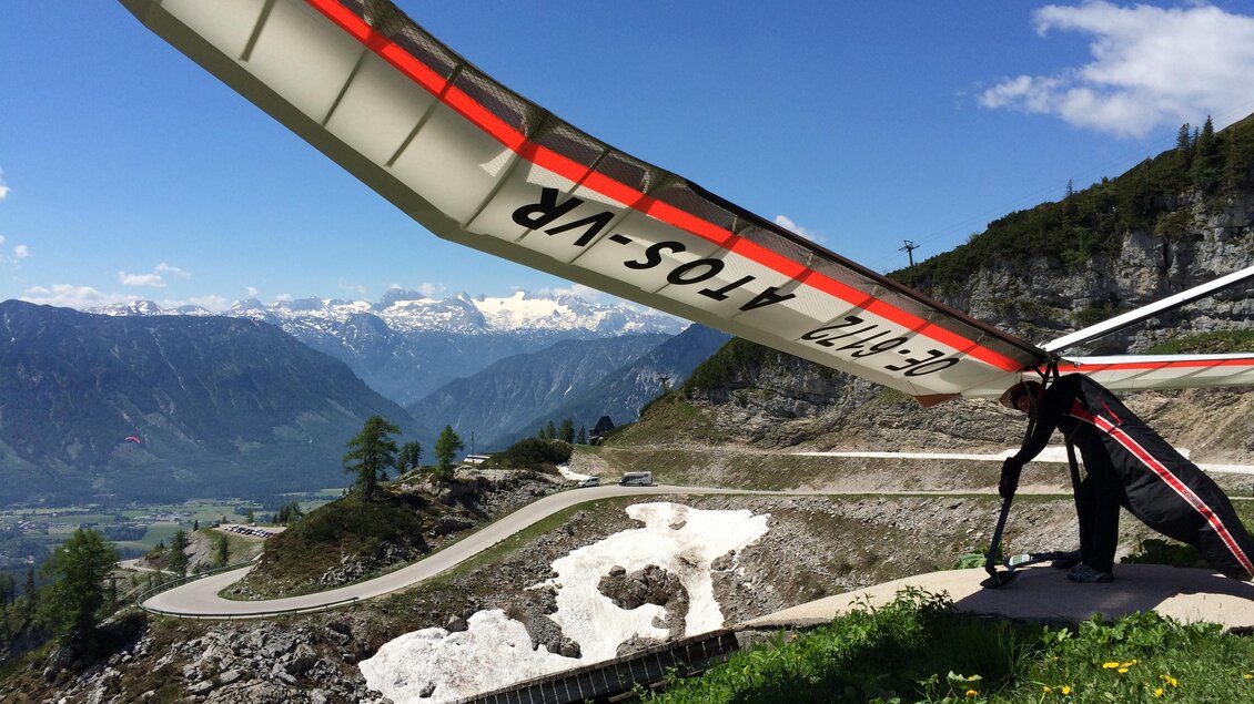 <p>Ein Drachenflieger steht am Rand des Berghangs am Loser mit Blick auf die umliegenden Berge des Ausseerlandes und auch den Dachstein. Der Himmel ist klar und blau, ideal für das Fliegen.</p> | © Loser Bergbahnen/M. Raich