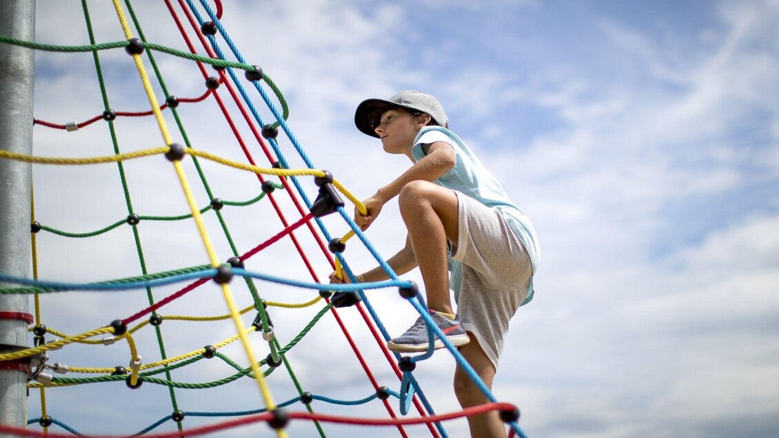 <p>Ein Junge klettert auf ein Spielgerüst aus bunten Seilen am Spielplatz neben der Loseralm in Altaussee. Der Himmel über dem Ausseerland ist bewölkt.</p> | © TVB Ausseerland - Salzkammergut-Tom Lamm