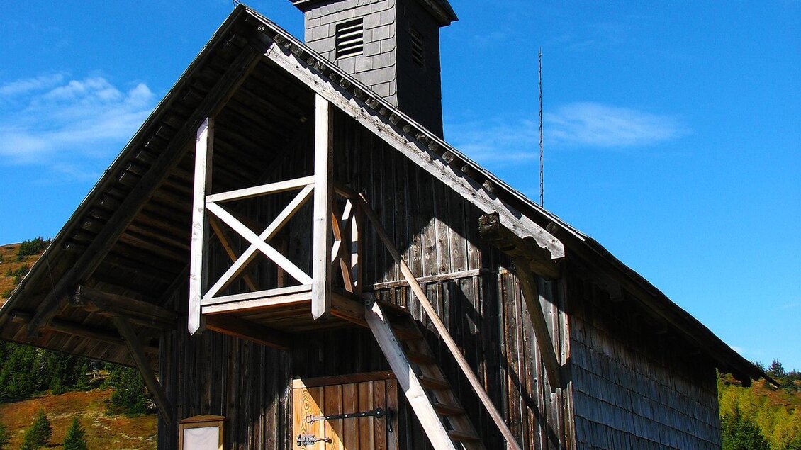 Eine kleine Holzkapelle mit einem Glockenturm und einer Treppe. Der Himmel ist blau und es gibt eine schöne Landschaft im Hintergrund. | © Wolfgang Mitteregger