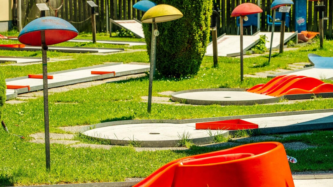 Eine Minigolf-Anlage mit bunten Schirmen und verschiedenen Spielbahnen. Die grüne Wiese und die sonnige Atmosphäre laden zum Spielen ein. | © Wolfgang Spekner