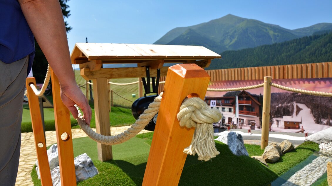 Eine Miniaturlandschaft mit einer Holzkonstruktion und einem Drahtseil. Im Hintergrund sind Berge und eine malerische alpine Szenerie zu sehen. | © Mountain Adventure Golf