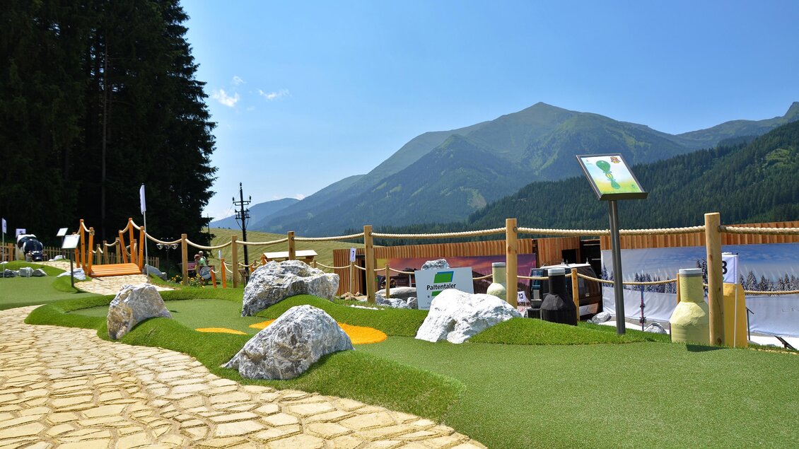 Ein schöner Aussichtspunkt am See mit einem gepflegten Weg. Im Hintergrund sind grüne Berge und ein klarer Himmel zu sehen. | © Mountain Adventure Golf