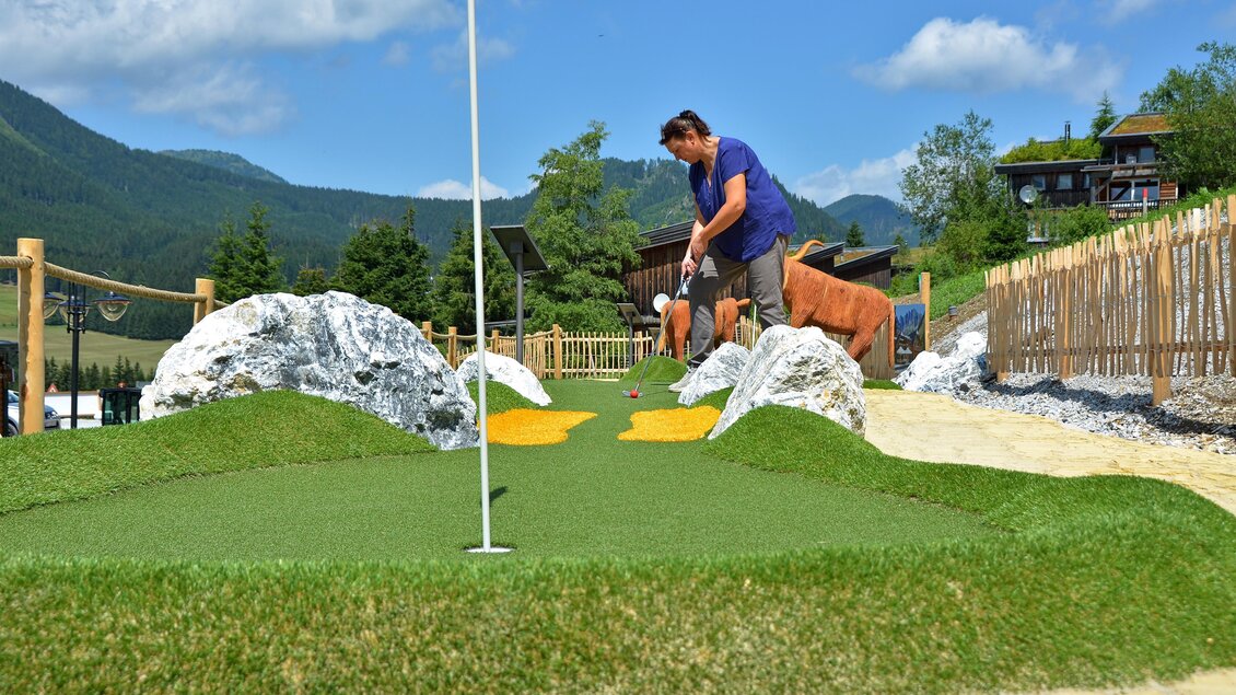 Eine Minigolfanlage mit grünen Rasenflächen und Felsen. Im Hintergrund sind Berge und eine Holzlattenzaun zu sehen. | © Mountain Adventure Golf