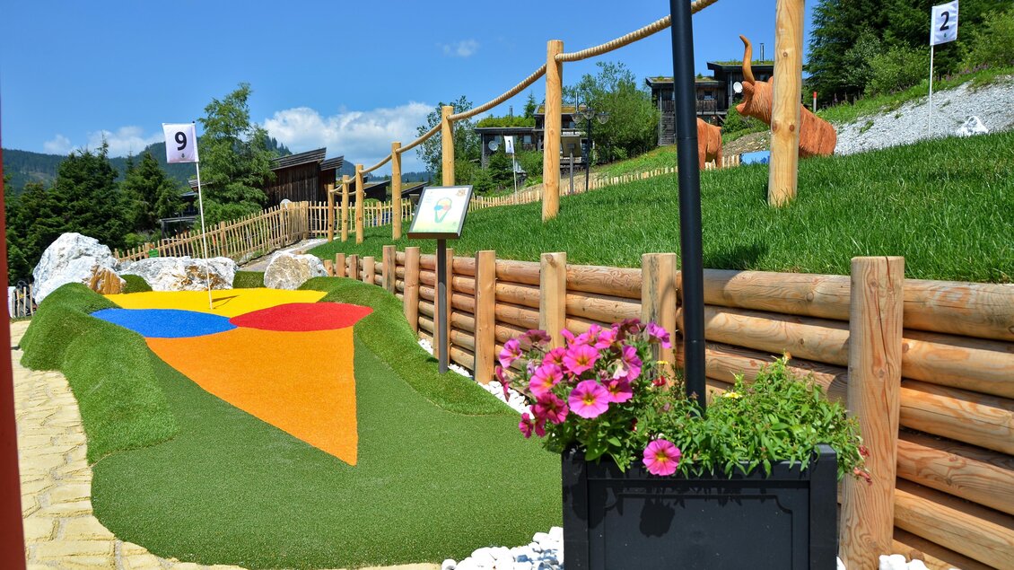 Ein Minigolfplatz mit bunten Hindernissen und einem gepflegten Rasen. Im Hintergrund sind Holzverkleidungen und grüne Bäume sichtbar. | © Mountain Adventure Golf