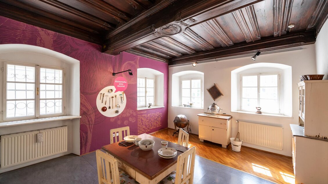 Ein gemütlicher Essbereich mit einem Holztisch und vier Stühlen. Die Wände sind teilweise lila gestrichen, und es gibt große Fenster, die viel Licht hereinlassen. | © Stadtgemeinde Kapfenberg