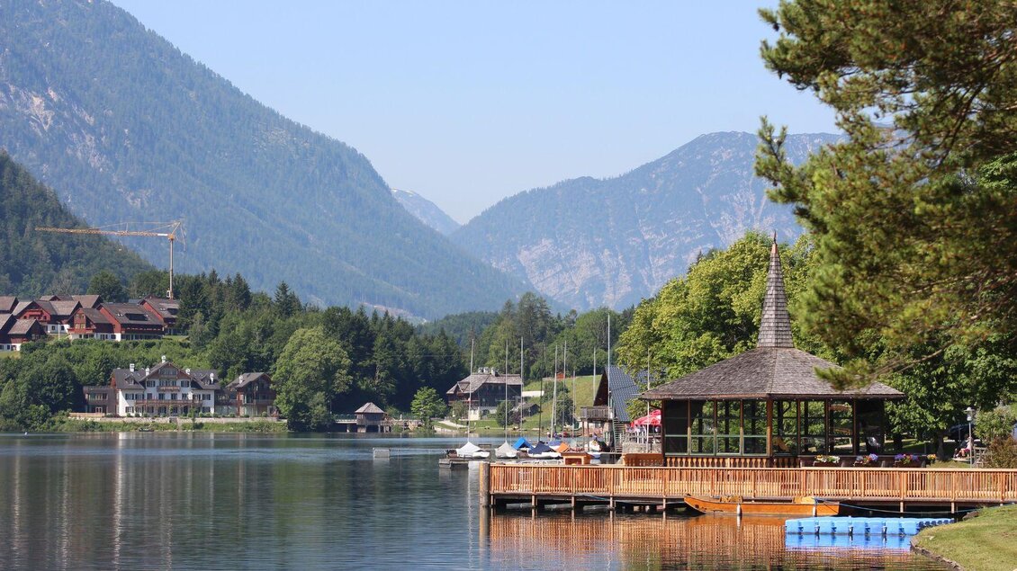 Ein malerischer See umgeben von Bergen. Im Vordergrund steht ein Holzsteg mit einem Pavillon. | © Viola Lechner