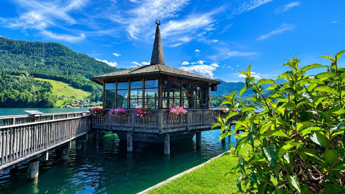 <p>Der Musikpavillon im Gemeindepark Grundlsee liegt idyllisch am Wasser, umgeben von blühenden Pflanzen und der grünen Berglandschaft. Unter dem klaren blauen Himmel lädt dieser besondere Ort zum Verweilen und Genießen ein. In den Sommermonaten finden an den Donnerstagen Konzerte der Musikkapelle Grundlsee statt.</p> | © Tourismusverband Ausseerland