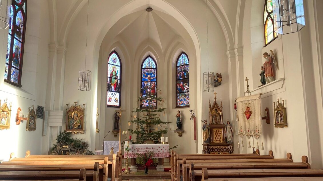 Eine helle Kirche mit hohen Fenstern und farbenfrohen Glasmalereien. In der Mitte steht ein Weihnachtsbaum und Bänke laden zum Sitzen ein. | © Bettina Scheck