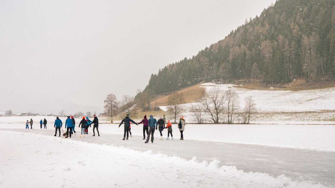 Ein winterlicher Sonnenuntergang über einer gefrorenen Landschaft. Menschen gehen auf einer Eisbahn in der ruhigen Umgebung. | © Christoph Lukas