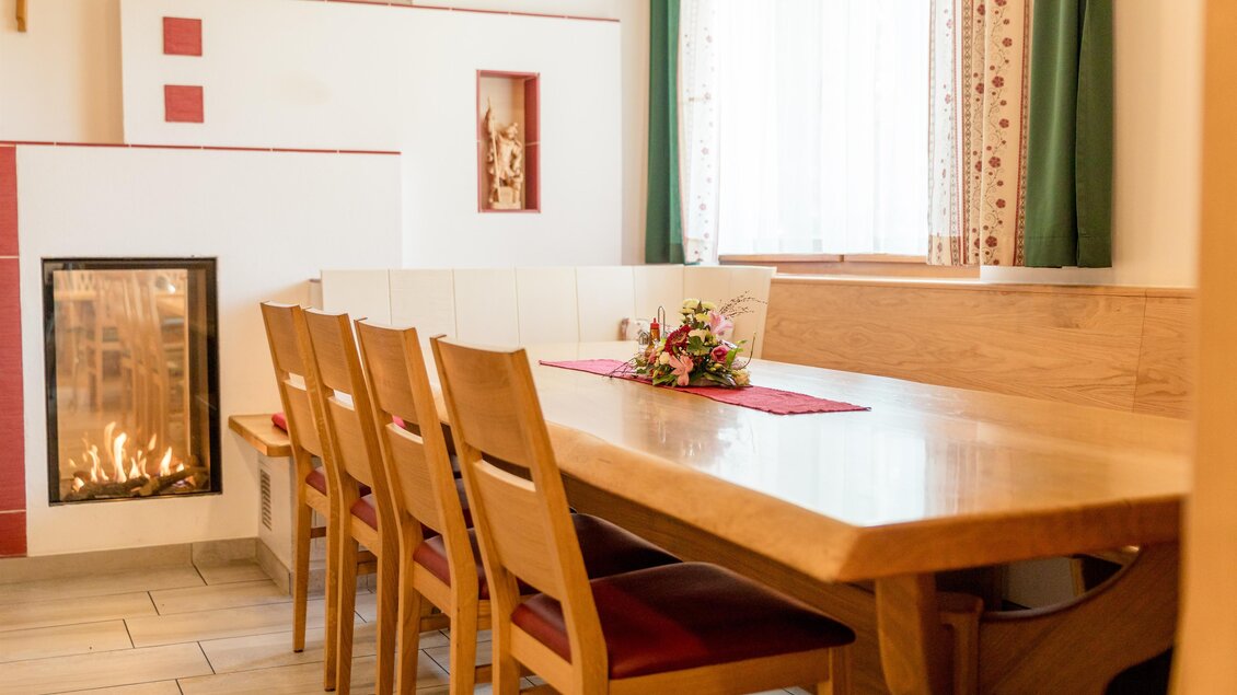Ein einladender Essbereich mit einem langen Holztisch und Stühlen. Im Hintergrund ist ein Kamin, der eine gemütliche Atmosphäre schafft. | © Restaurant Leitner
