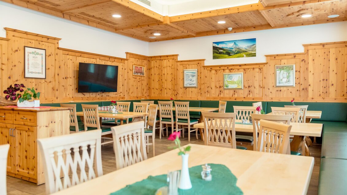 Ein gemütlicher Essraum mit holzverkleideten Wänden und grünen Bänken. Tische sind ordentlich gedeckt, und an der Wand hängen verschiedene Bilder. | © Restaurant Leitner