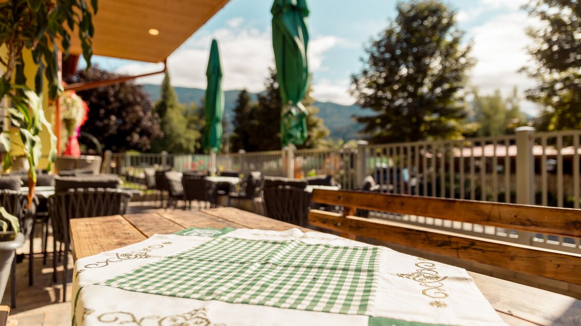 Ein gemütlicher Außenbereich mit Holztischen und grünen Sonnenschirmen. Im Hintergrund sind Bäume und eine Berglandschaft zu sehen. | © Restaurant Leitner