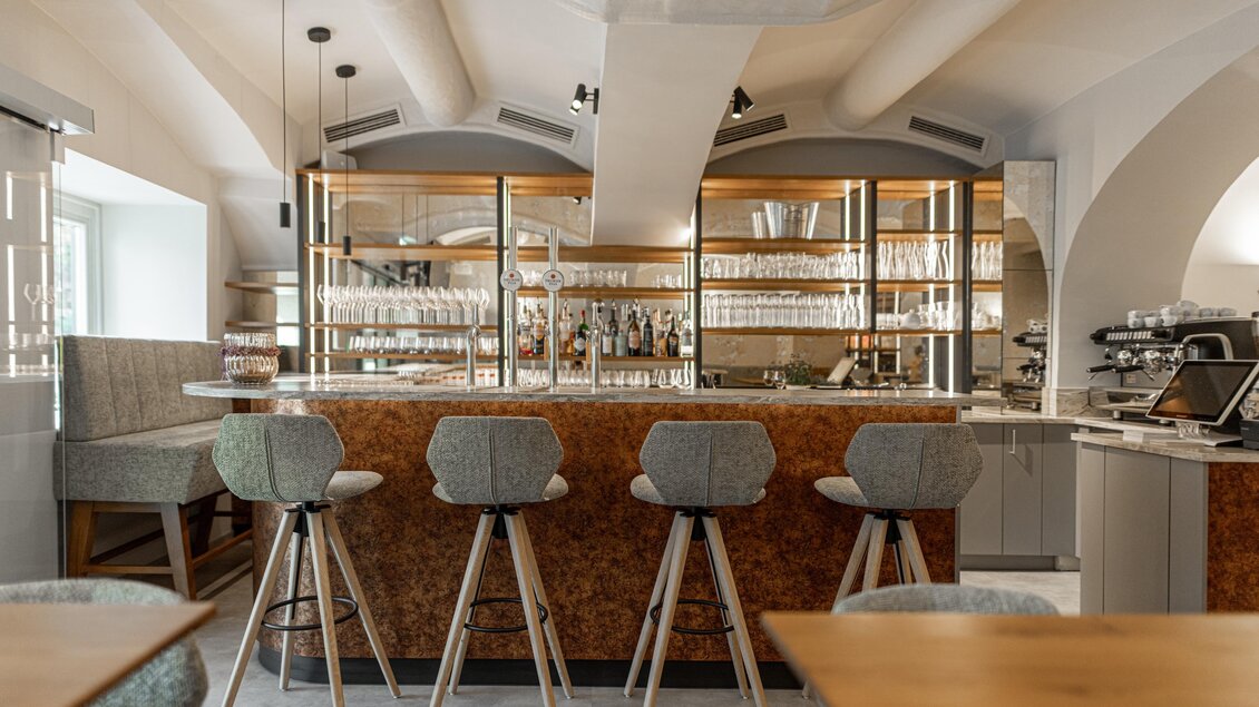 Bar im Restaurant Wörgötter in Ligist mit vier gepolsterten Barhockern, Zapfhähnen und beleuchteten Glasregalen | © Die Abbilderei