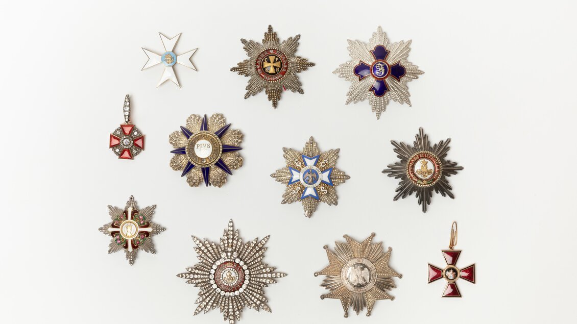 Eine Anordnung von verschiedenen Orden und Abzeichen auf einem weißen Hintergrund. Die Orden sind aus Metall und zeigen unterschiedliche Farben und Designs. | © Lipp Zahnschirm