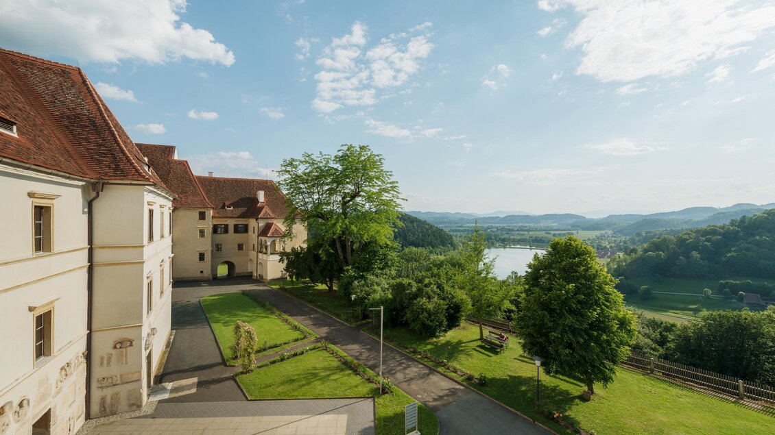 Eine malerische Landschaft mit einem historischen Gebäude und einer grünen Wiese. Im Hintergrund erstreckt sich ein ruhiger Fluss umgeben von sanften Hügeln. | © Stefan Kristoferitsch