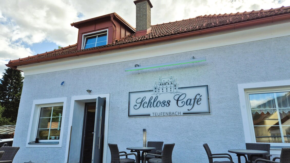 Ein einladendes Café mit dem Namen "Schloss Café" in Teufenbach. Die Fassade ist hell gestrichen und es stehen Tische draußen bereit. | © TV Murau