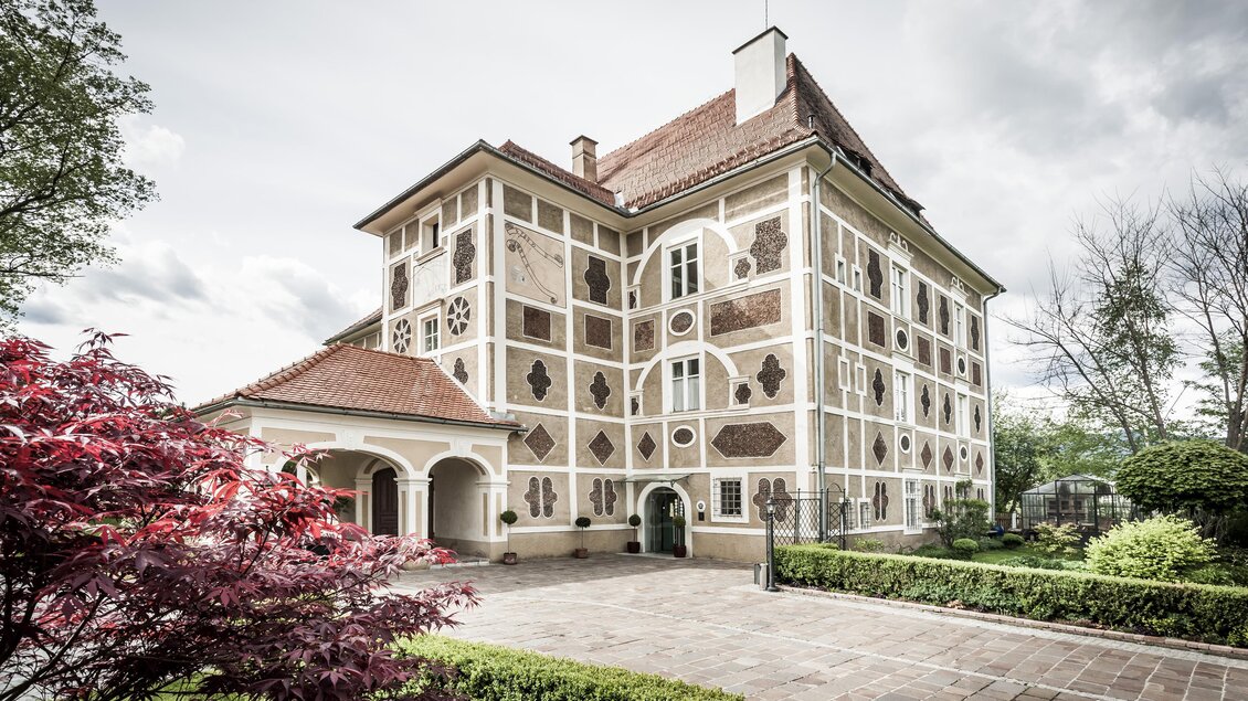 Ein elegantes Gebäude mit einzigartiger Fassadengestaltung. Umgeben von Grün und Blumen wirkt es einladend und charmant. | © Schloss Farrach
