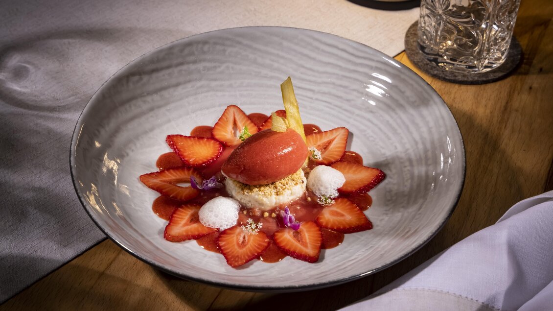 Ein kunstvoll angerichteter Dessertteller mit Erdbeeren und einem Sorbet. Das Gericht ist mit essbaren Blüten und einer kleinen Dekoration aus Mürbeteig verziert. | © Schloss Farrach