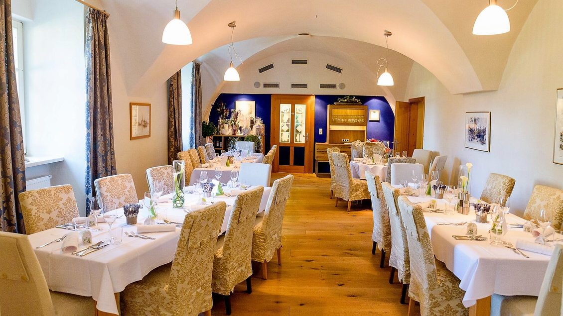 Ein eleganter Speisesaal mit Tischen, die für ein festliches Abendessen deckiert sind. Die Wände sind hell, und große Fenster lassen viel Licht herein. | © Schloss Farrach
