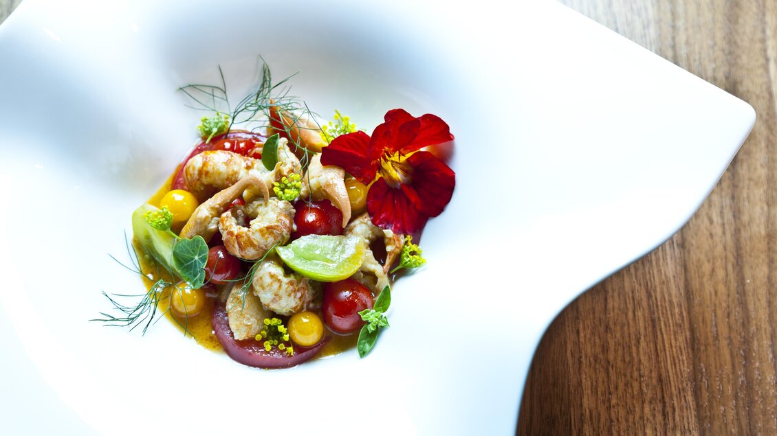 Ein kunstvoll angerichtetes Gericht auf einem weißen Teller. Es enthält frische Garnelen, bunte Tomaten und essbare Blüten. | © Schloss Farrach