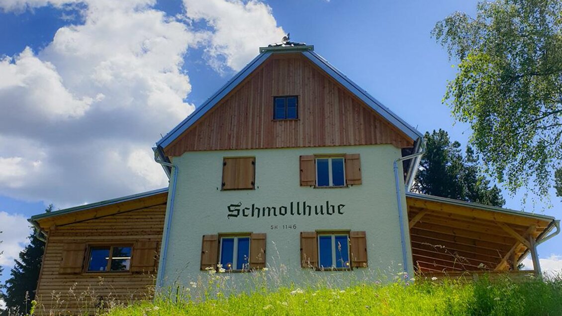 Ein charmantes Holzhaus mit der Aufschrift "Schmollhube". Das Gebäude steht auf einem Hügel unter einem klaren blauen Himmel. | © Stadtgemeinde Leoben - BÜKO
