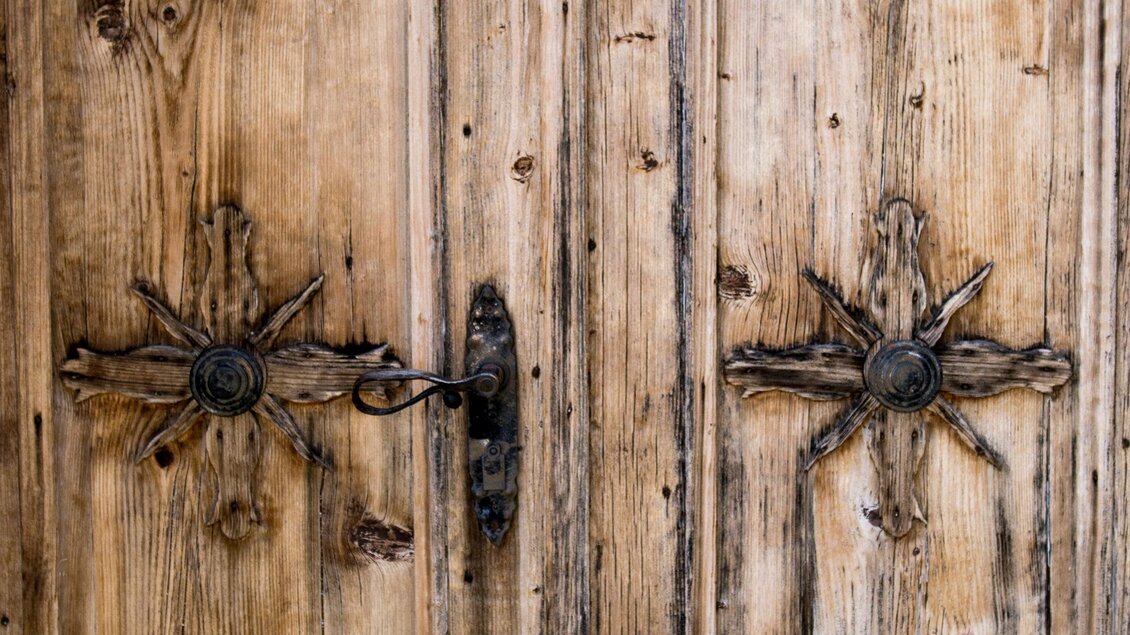 Eine alte Holztür mit kunstvollen Verzierungen und einer rustikalen Oberfläche. Die Tür hat einen historischen Charme und zeigt feine Details in der Holzarbeit. | © Anita Fössl