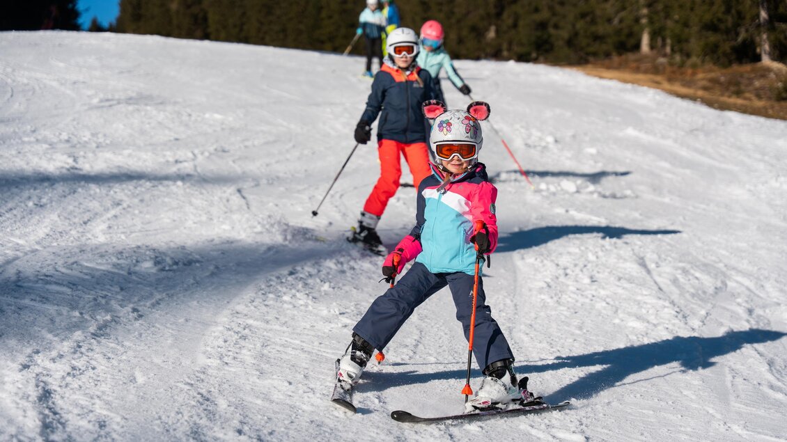 Kinder die in einer Schlange im Schnee mit ihren Skiern die Piste runterfahren. | © Cian Baumgartner