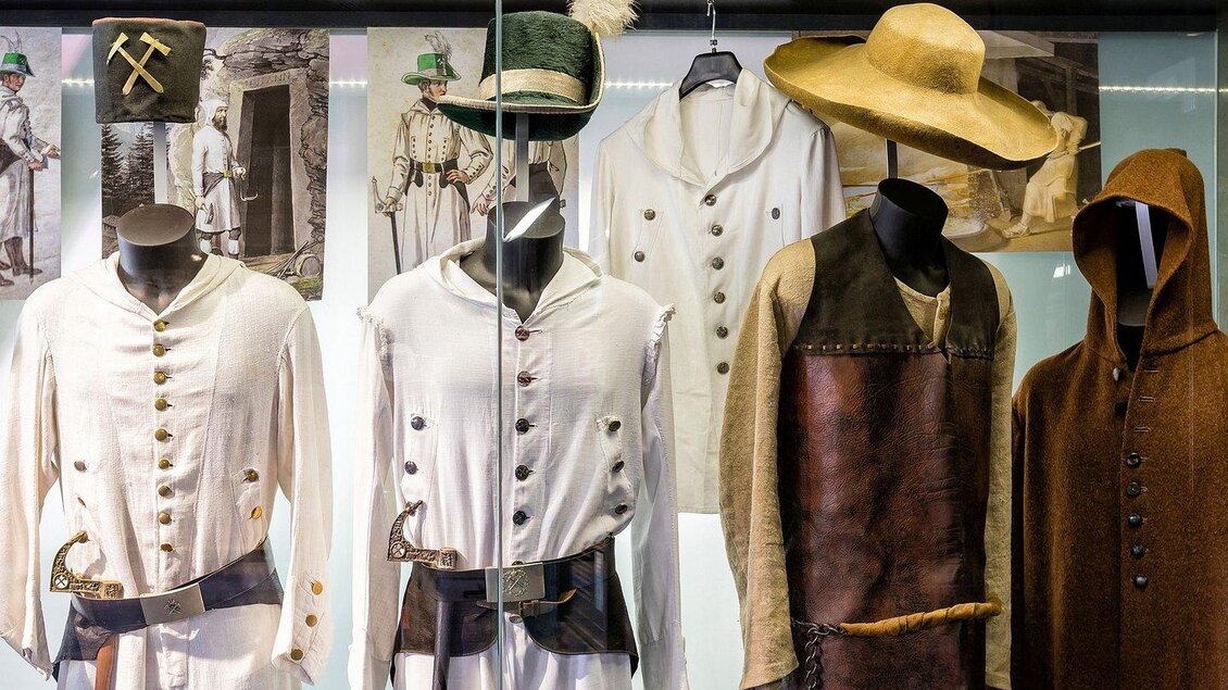 Eine Ausstellung von historischen Arbeitskleidungen in einer Vitrine. Die Kleidung umfasst verschiedene Modelle und Materialien, dargestellt an Schaufensterpuppen. | © Museumsverbund