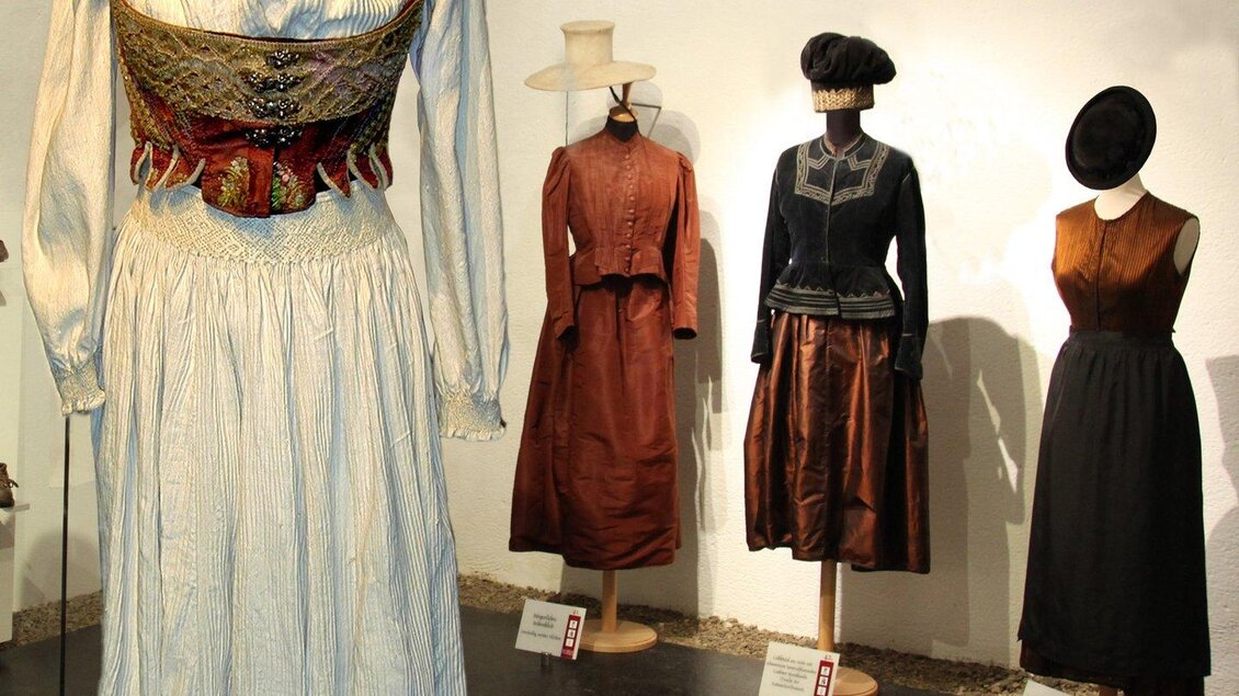 Eine Ausstellung von traditionellen Kleiderstücken in einem Museum. Die Kleidungsstücke sind auf Ständern drapiert und zeigen verschiedene historische Stile. | © Museumsverbund Betriebsges.m.b.H.