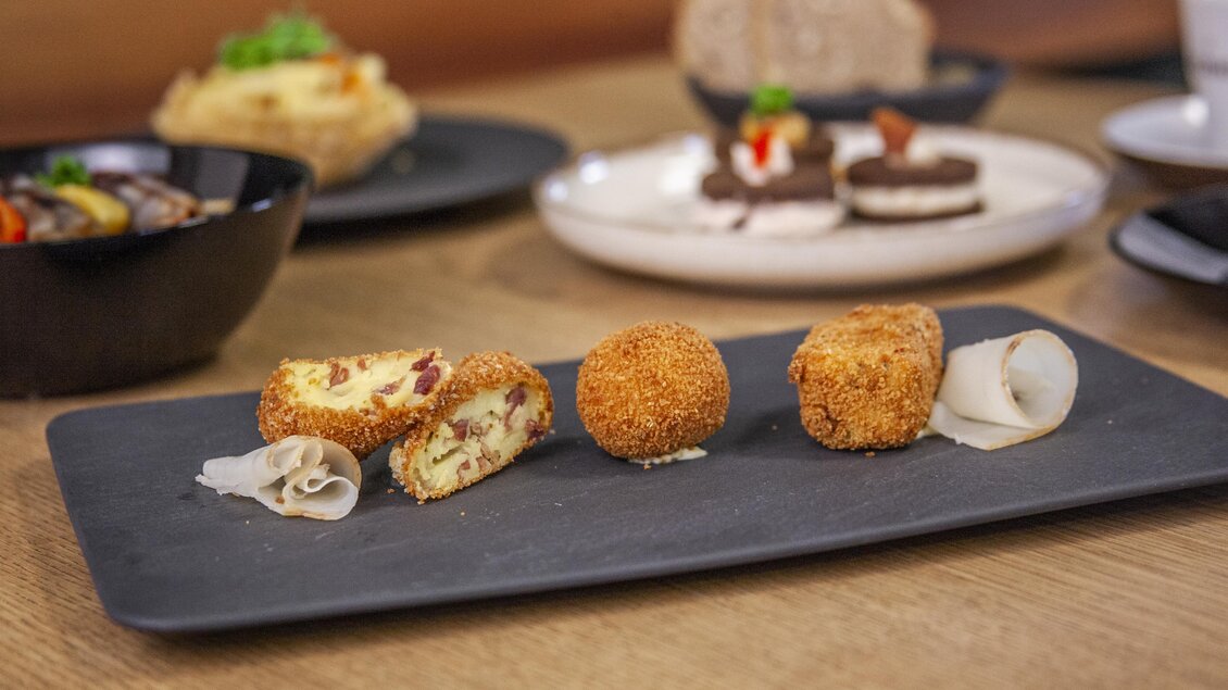 Eine Auswahl an frittierten Snacks auf einer Servierplatte. Neben den Snacks befinden sich verschiedene Schalen mit weiteren Speisen. | © Vulcano